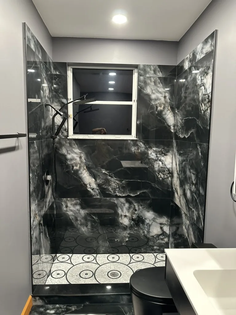 Finished walk-in shower with dark large-format tile and circular mosaic floor