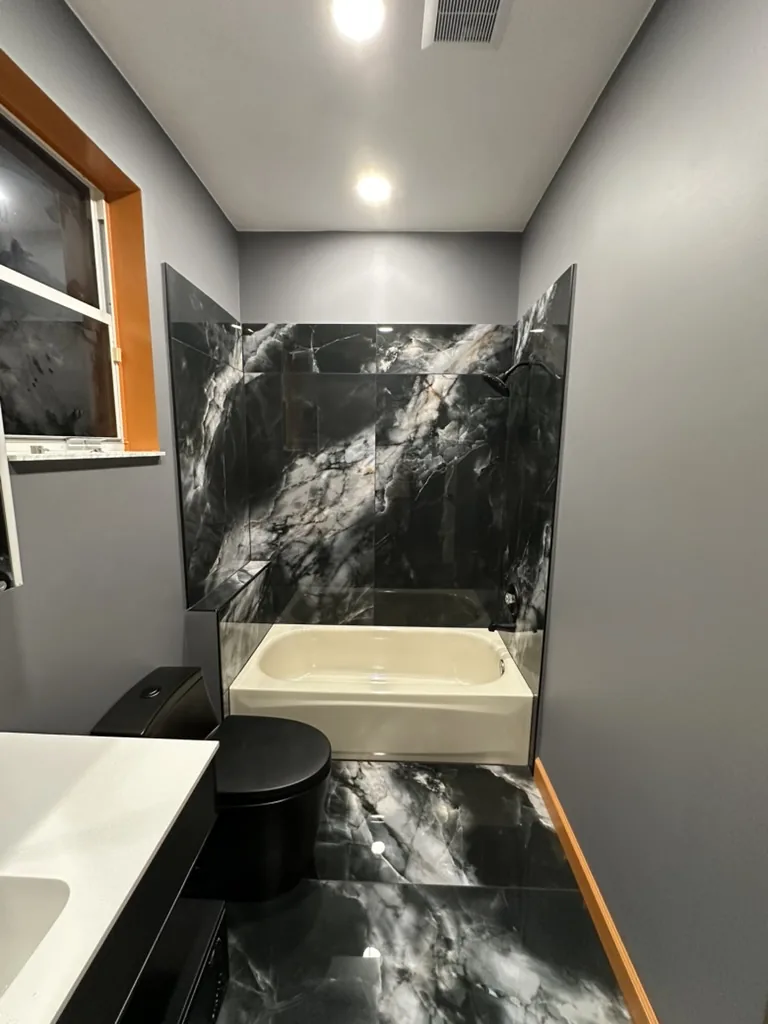 Finished tub bathroom with black marble-look tile and gray painted walls