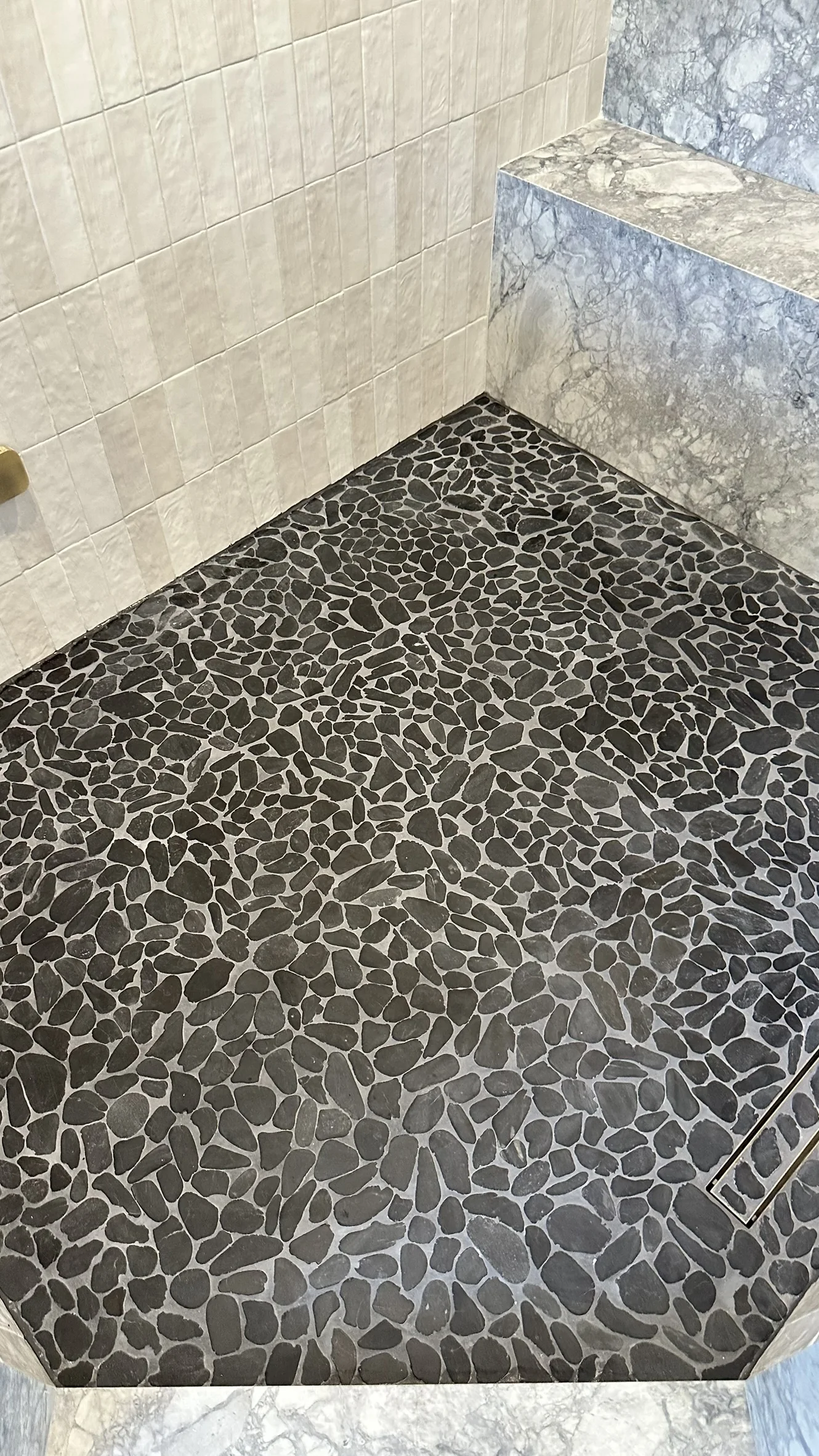 Dry dark pebble mosaic and gray grout detail at the shower perimeter