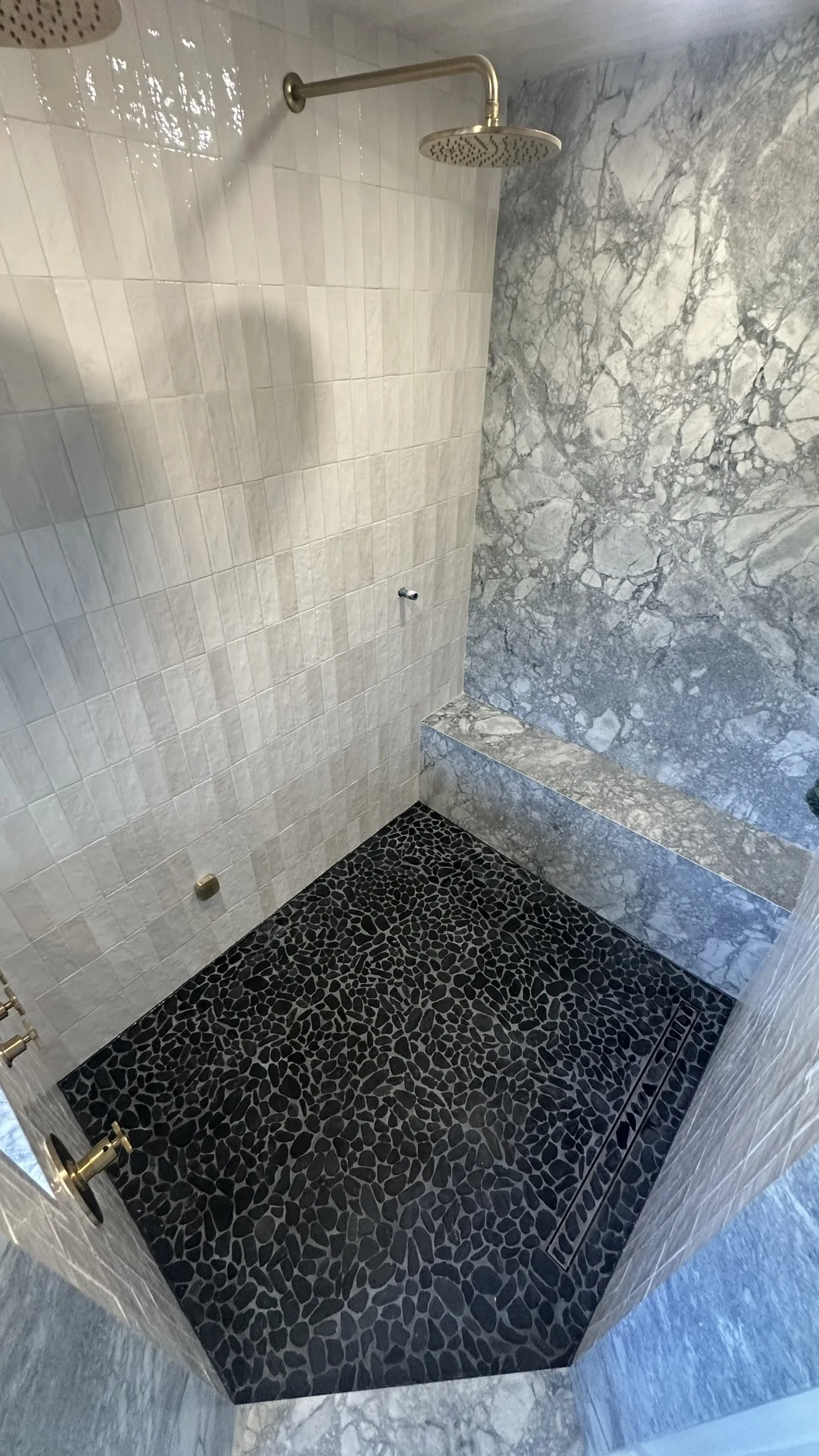 Finished dark mosaic shower floor with surrounding light wall and bench finishes