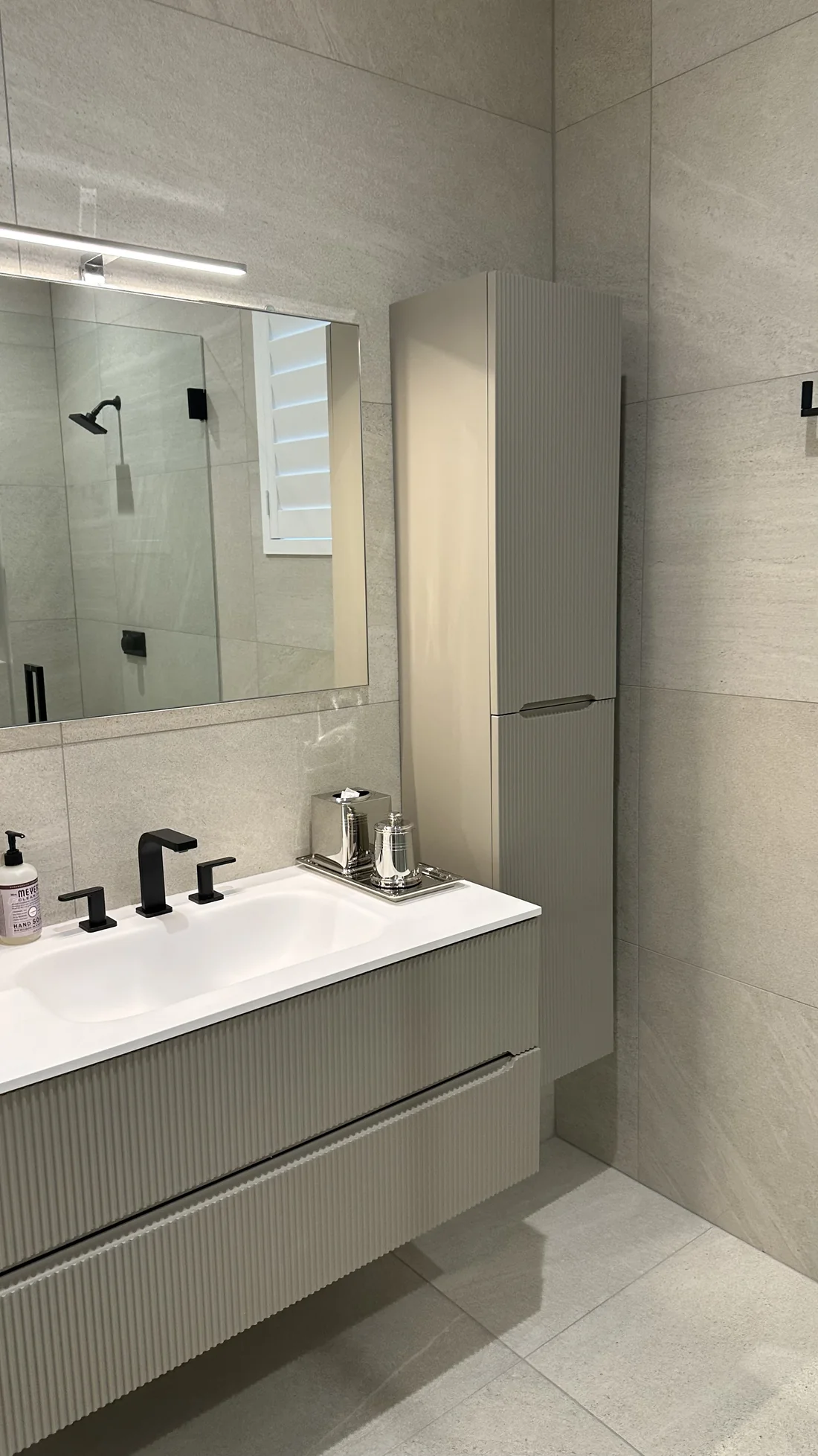 Wall-mounted bathroom vanity, mirror, and tall storage cabinets against tiled walls