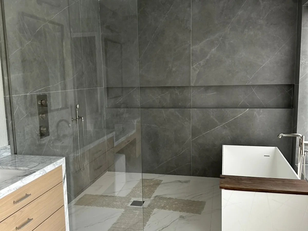 Modern bathroom with gray tile, glass shower, freestanding tub, and wood vanity