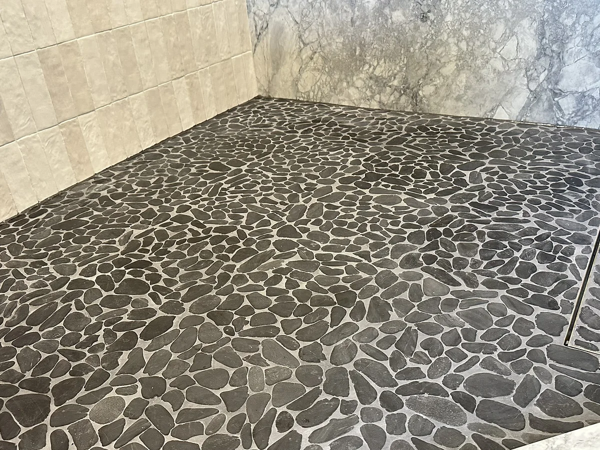 Dark pebble mosaic shower floor with a linear drain